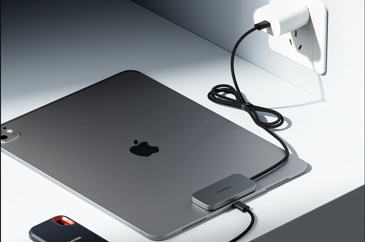 Apple laptop with magnetic attachment with cables leading to the wall and to a phone.